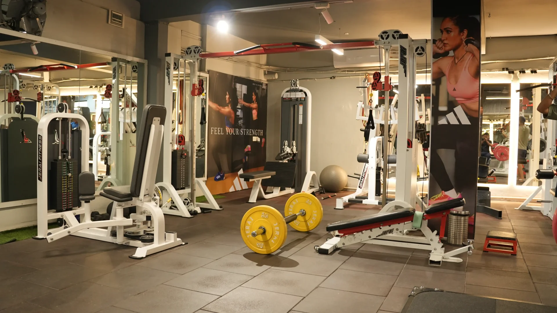 Strength training floor with barbell, cable machines, and Feel Your Strength banner
